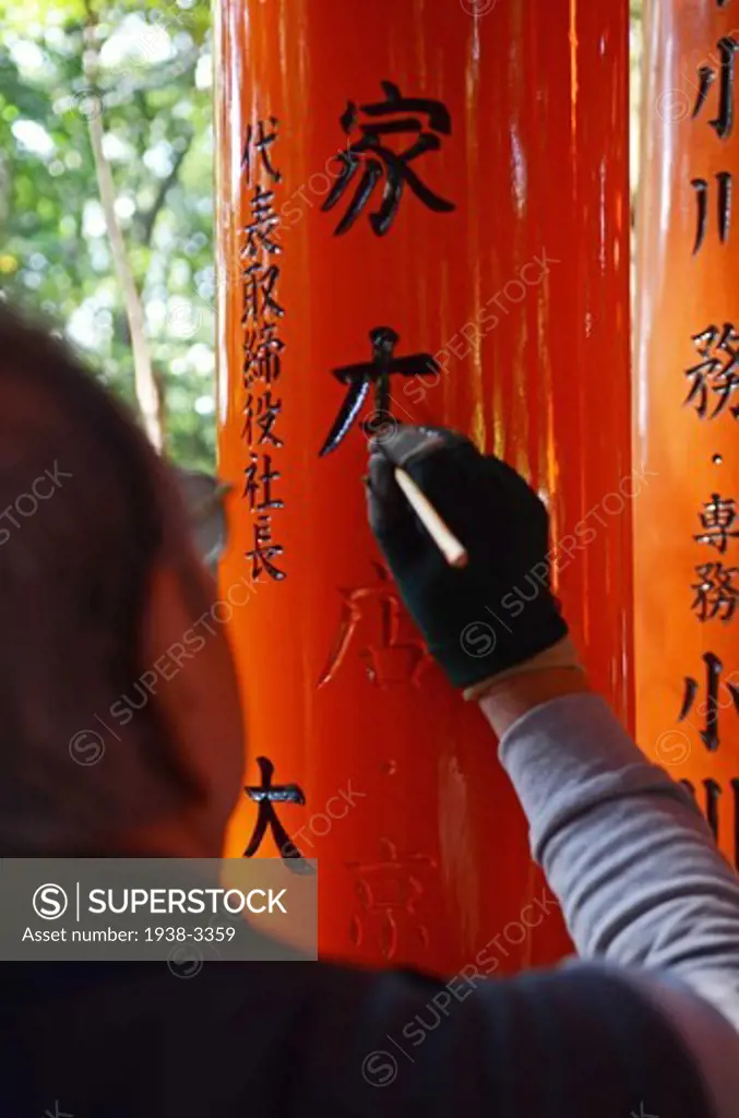 Restorer painting letters of a Torii gate at Fushimi Inari-Taisha shrine, Kyoto City, Honshu, Japan