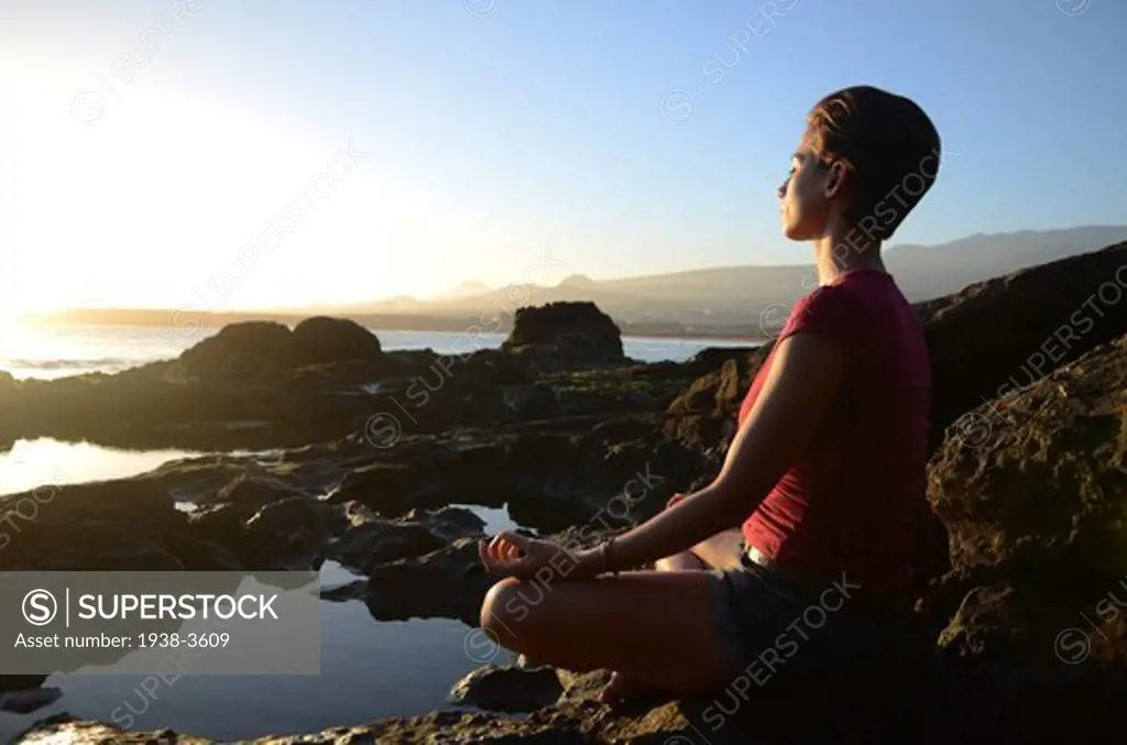 Young attractive woman meditates in lotus pose, in front of the coast.
