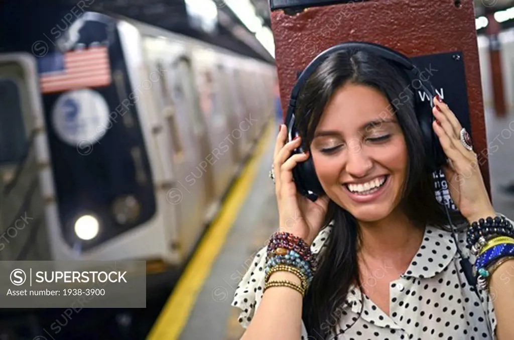 Attractive young mixed race woman listening to music in subway station, New York City