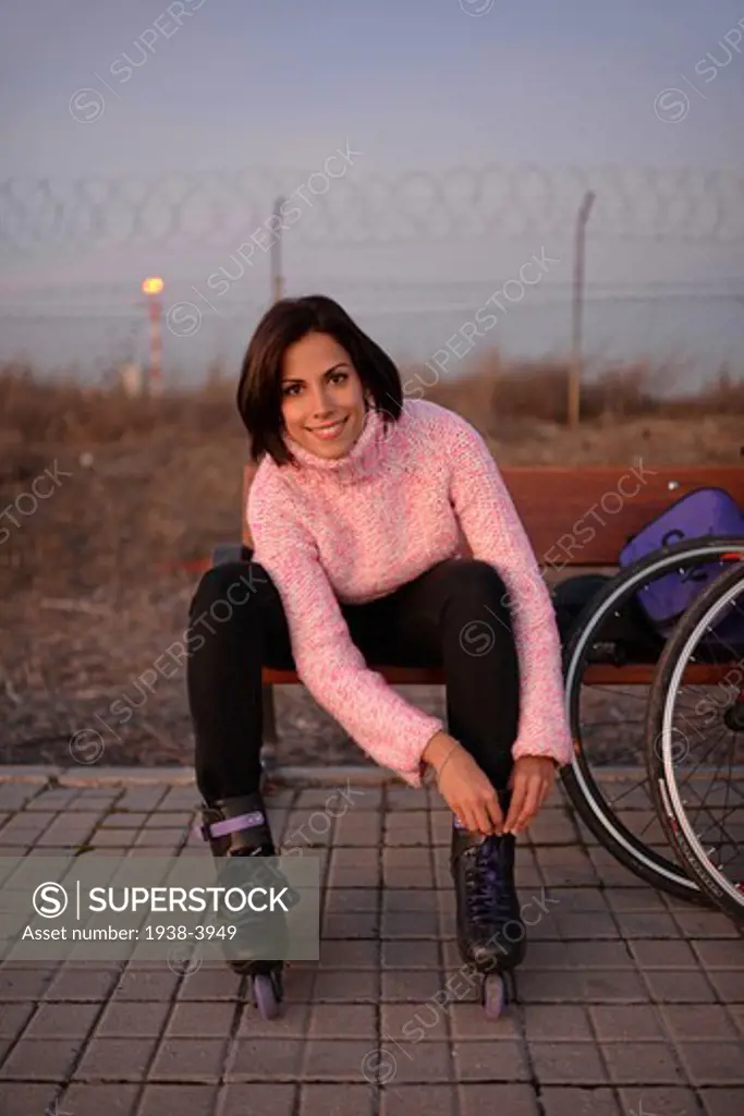 Young attractive woman puts rollerblades on at sunset