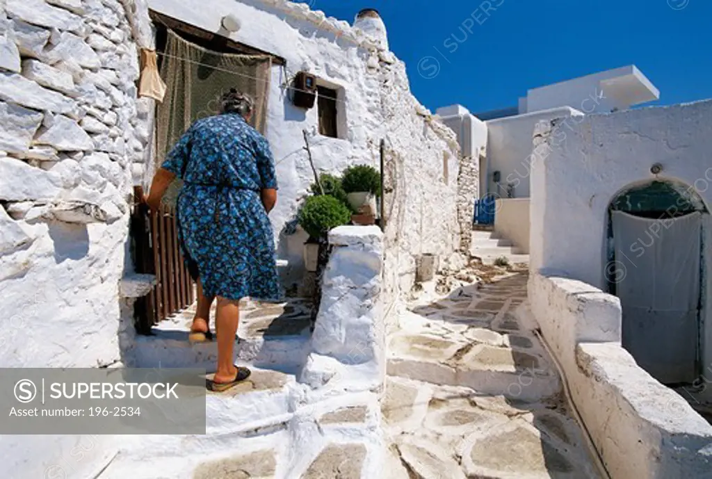 Greece, Cyclades, Sikinos, Woman walking in front of traditional house