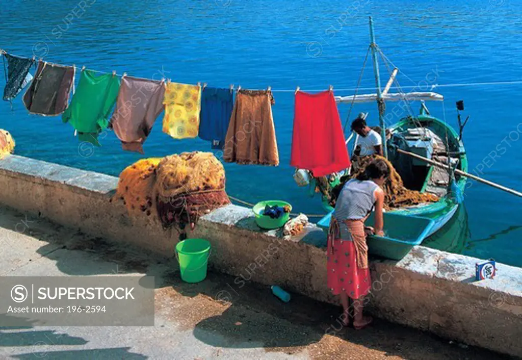 Greece, Ithaka, Woman doing laundry, men in fishing boat