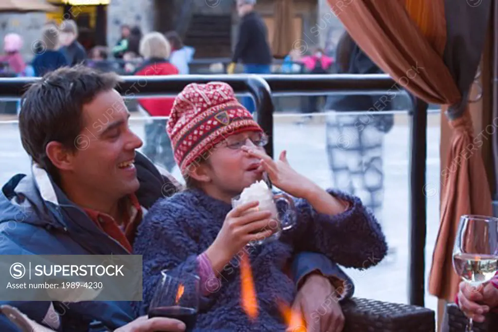A father and daughter drinking hot chocolate next to an ice skating rink