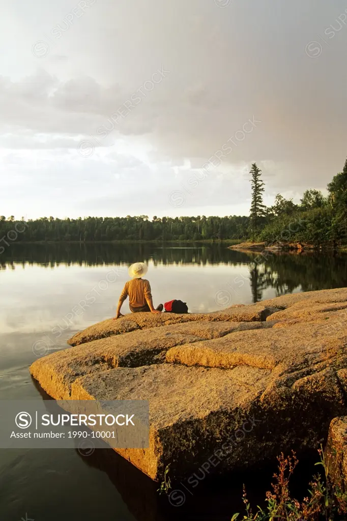 Hiker relaxing on shield rock along Numau Lake, Whiteshell Provincial Park, Manitoba, Canada.