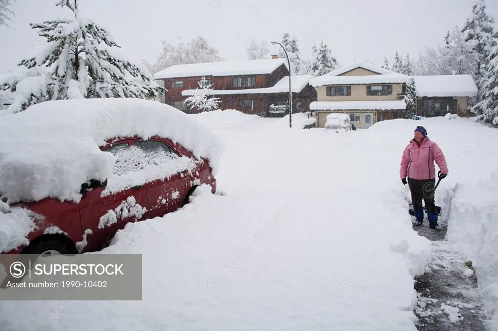 Woman shovelling driveway of snow after storm, Smithers, British Columbia