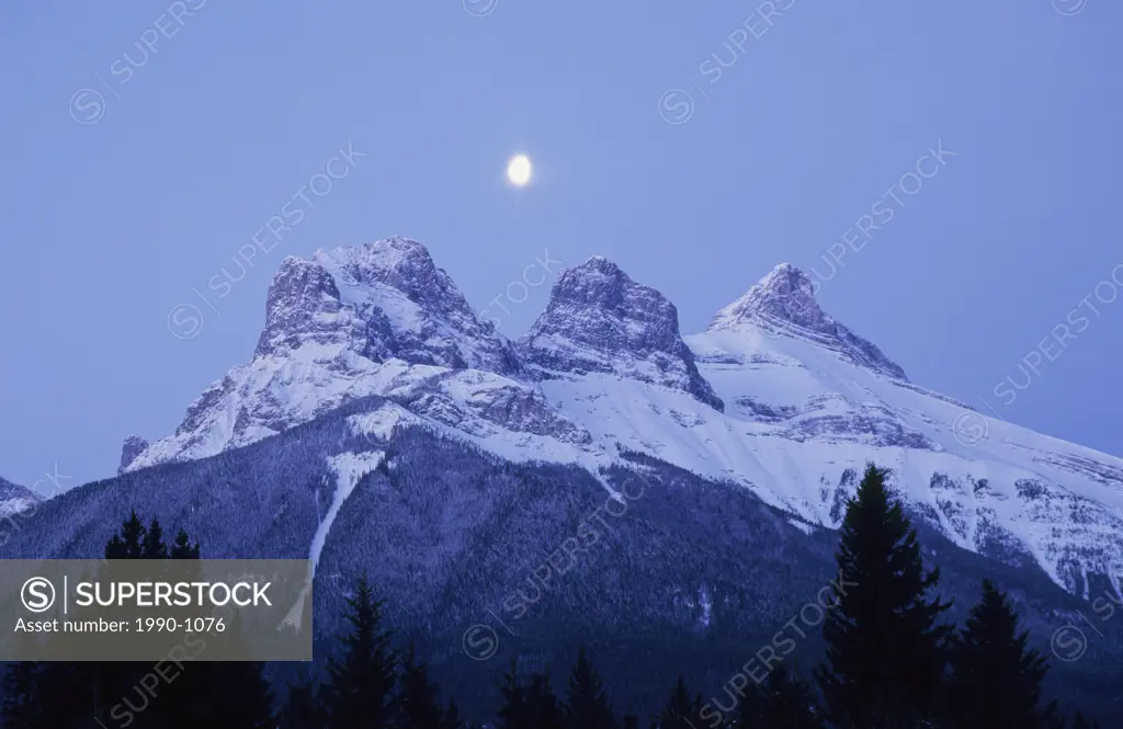 Moon rising over the Three Sisters Mountains at dusk, Canmore, Alberta, Canada