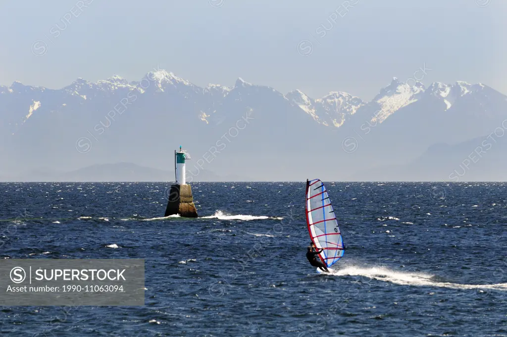 A windsurfer heads towards a marine marker in the Strait of Georgia near Pipers Lagoon in Nanaimo, BC. The coastal mountains on British Columbia are i...