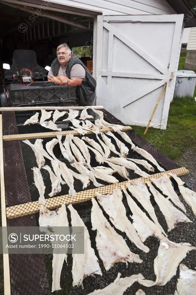 Man standing beside fish drying rack, Newfoundland, Canada