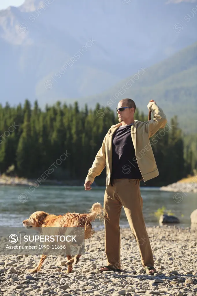 Young man plays fetch with his dog by a river in the mountains, British Columbia, Canada.