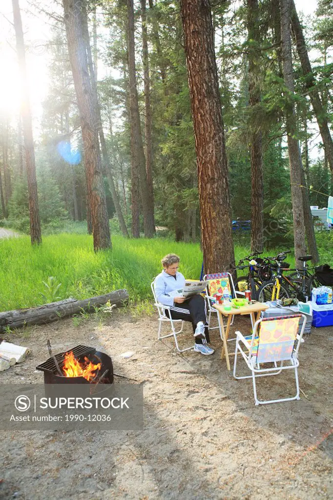 Reading by the fire in campsite, Kettle River, Provincial Park, Rock Creek, British Columbia, Canada.