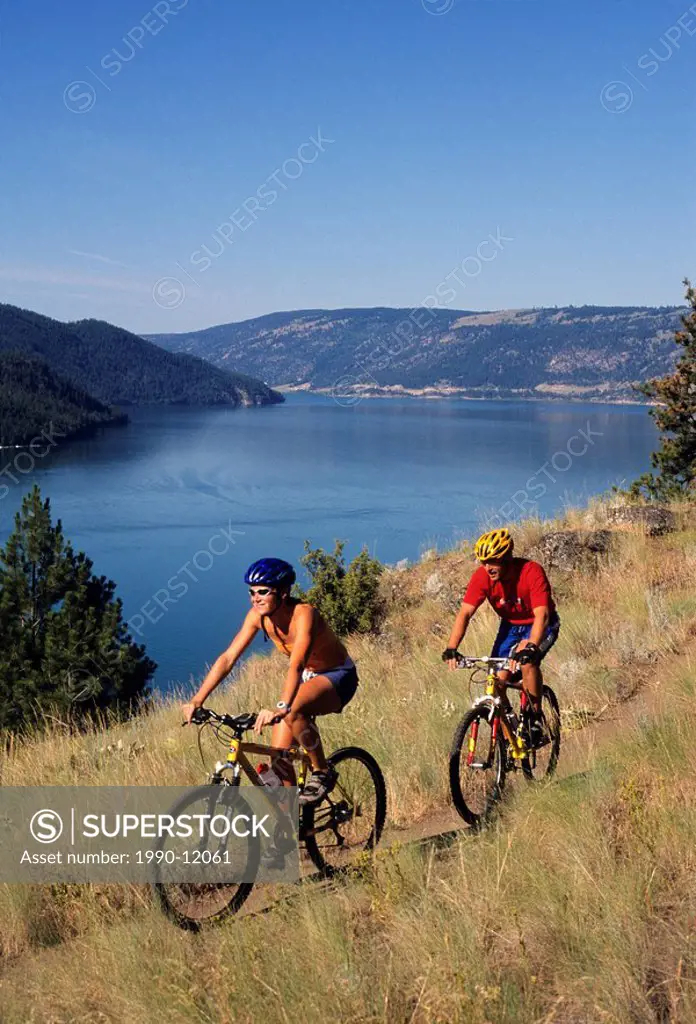 Young couple mountain biking with Kalamalka Lake in background, Kalamalka Provincial Park, British Columbia, Canada.