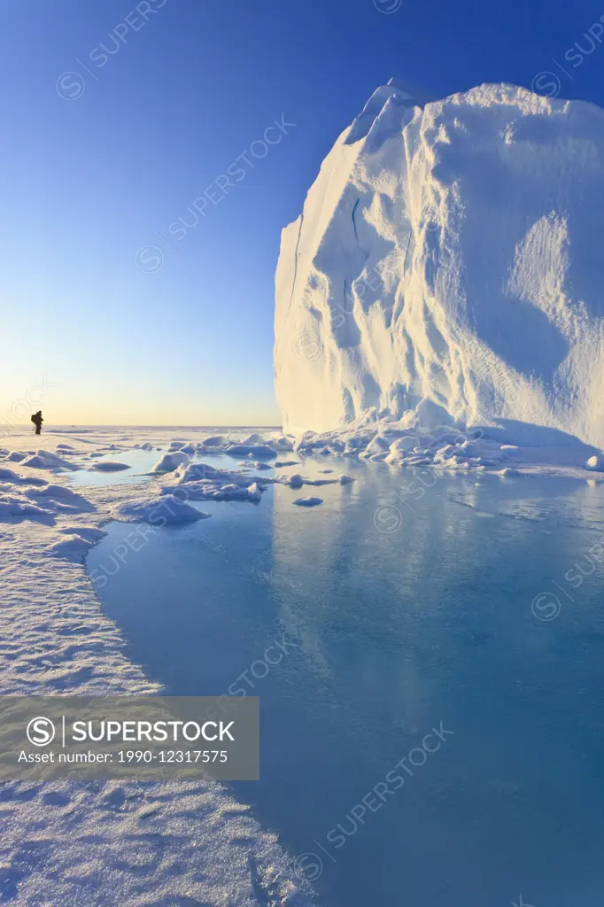 Human standing beside an iceberg in Baffin Bay on the Arctic Ocean, north of Baffin Island, Nunavut, Canada in the Canadian Arctic