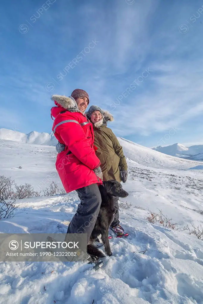 Happy couple standing with their dog on a hill along the DempsterHighway, Yukon after snowshoeing to the top.
