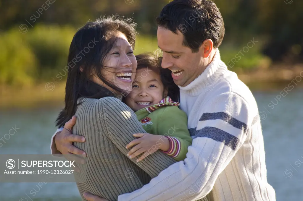 An asian mom and caucasian dad play with their daughter at Green Lake, Whistler.