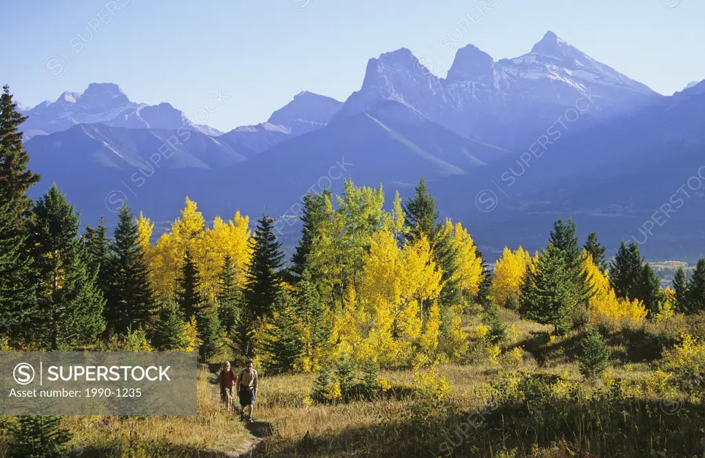 Hikers along a mountain trail in fall colours with the Three Sisters in the background, Canmore, Alberta, Canada