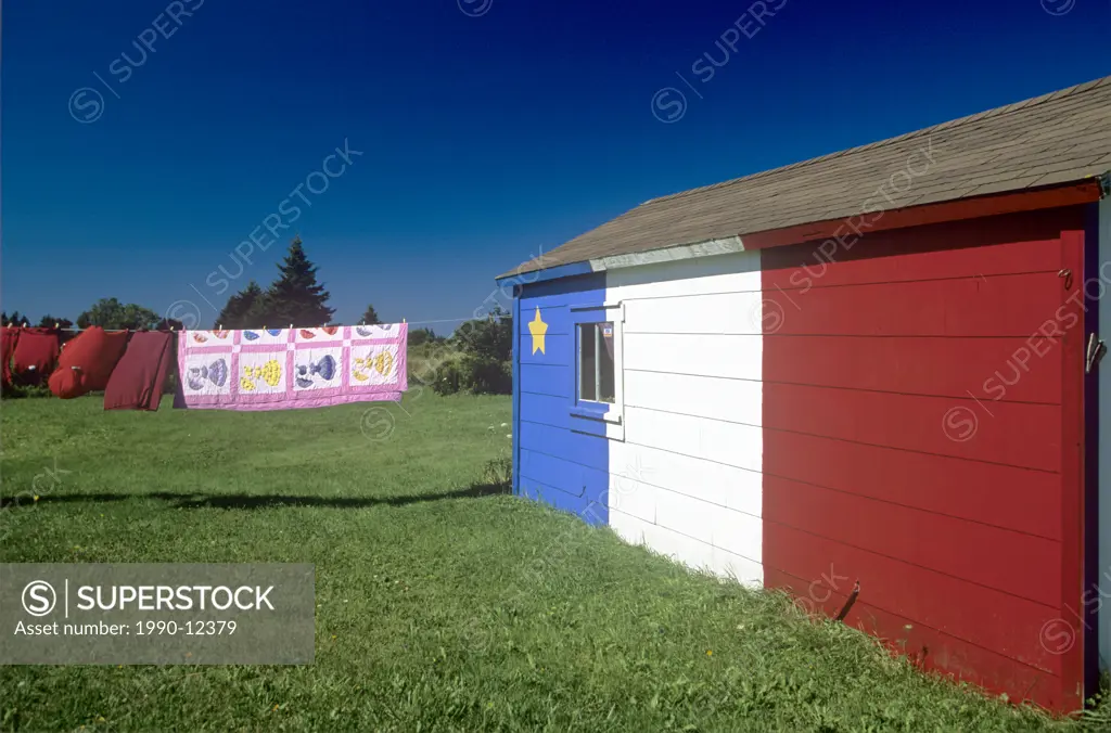 Quilt hanging on clothes line and Acadian flag painted barn, St. Bernard, Nova Scotia, Canada