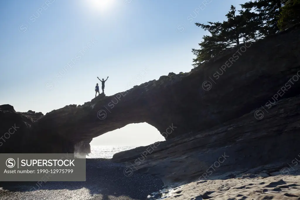 Two hikers stand on top of the sea arch at Tsusiat Point known as the 'Hole in the Wall'. West Coast Trail, Pacific Rim National Park Reserve, Vancouv...