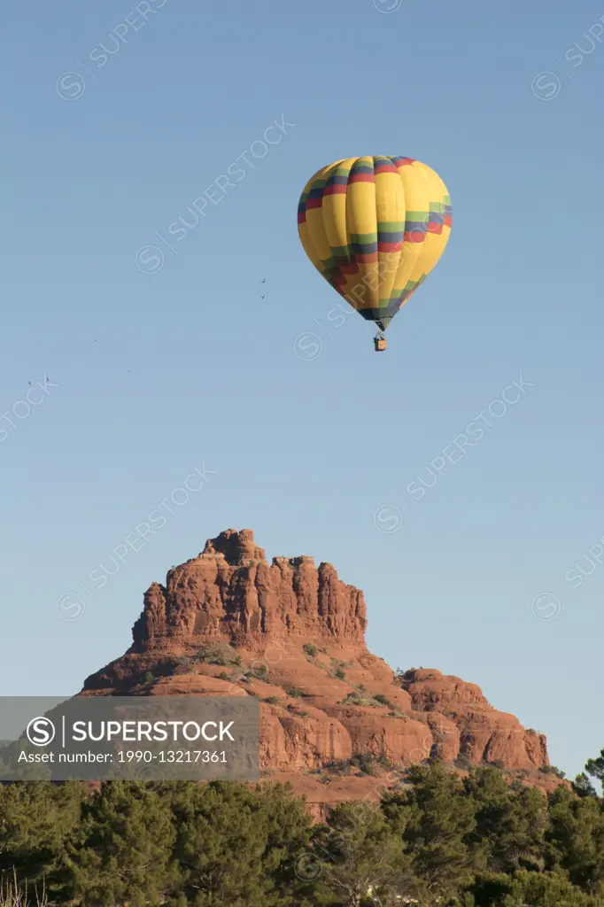 Hot air balloon flying near red rock formation known as Bell Rock, Coconino National Forest, Sedona, AZ