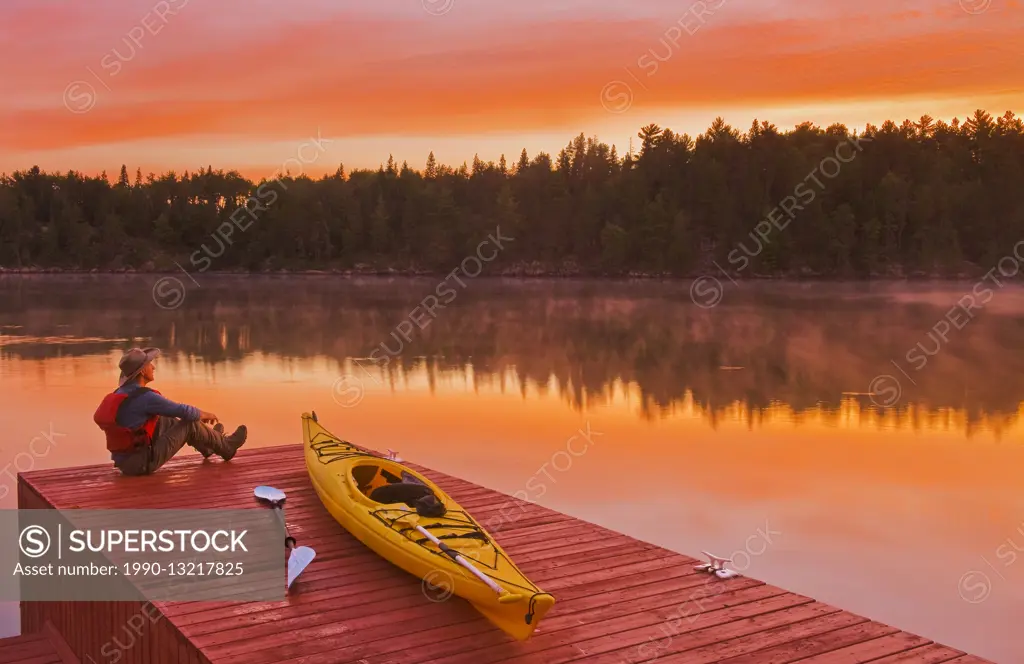 man next to kayak on on dock at sunrise, Lake of the Woods, Northwestern Ontario, Canada