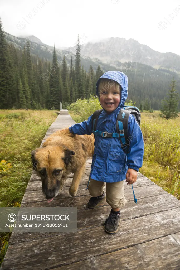 A happy toddler (boy) and his dog hikes on a boardwalk around Gibson Lake in Kokanee Glacier Provincial Park, British Columbia