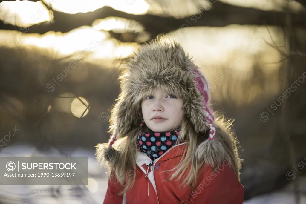 Girl (10) sitting in a tree on the shore of a frozen lake in winter.