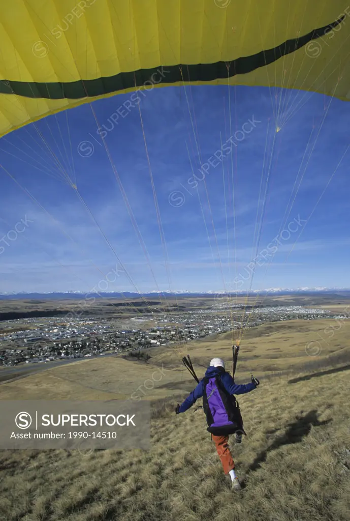 A paraglider landing on a grassy field in Cochrane, Alberta, Canada