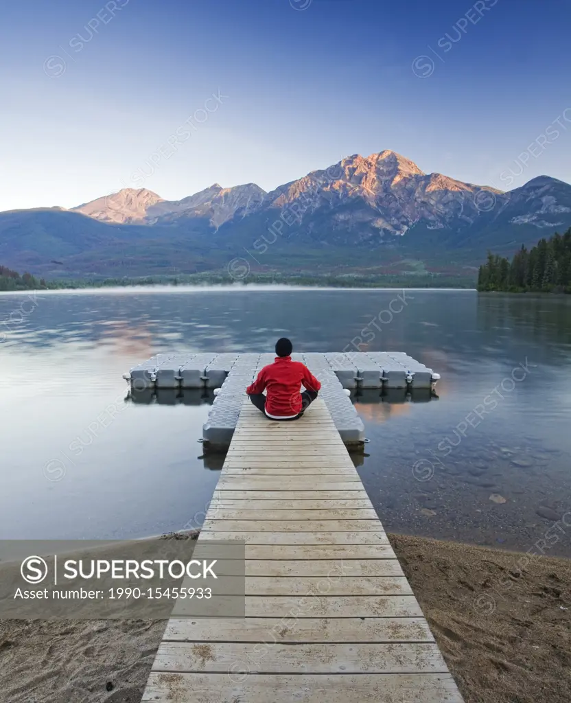 Man sitting on dock meditating at Pyramid Lake, Jasper National Park, Alberta, Canada.