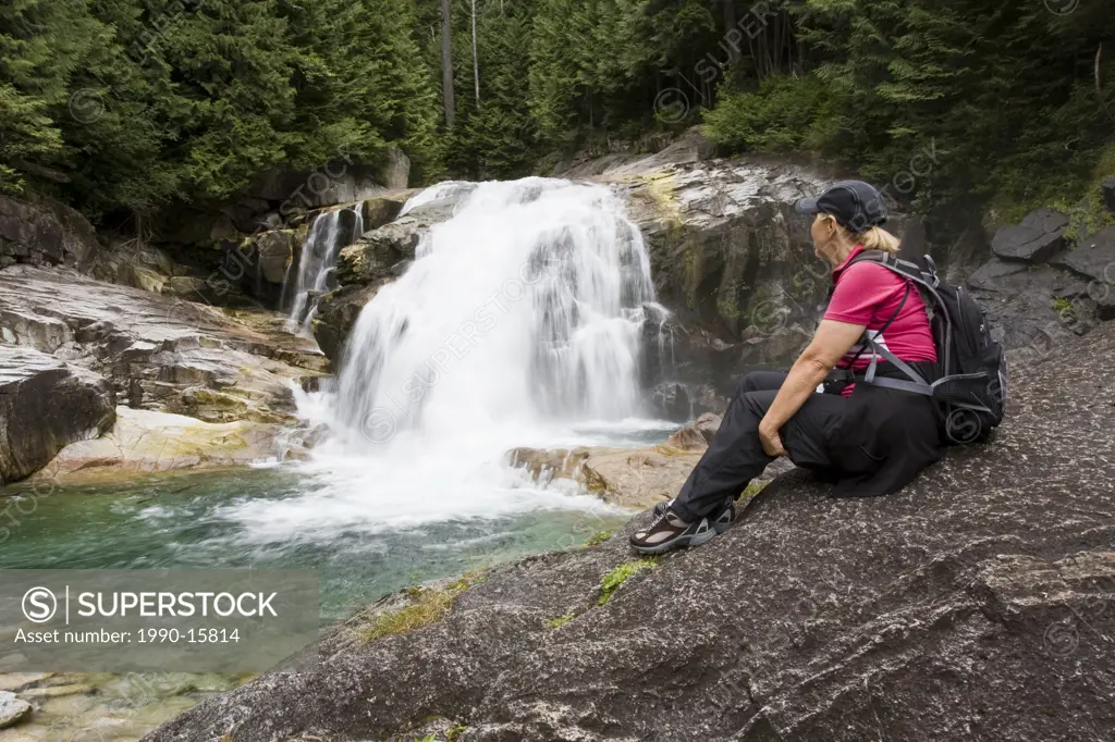 Woman hiker sitting on rock looking at waterfalls in Golden Ears Provincial Park in Maple Ridge, British Columbia, Canada