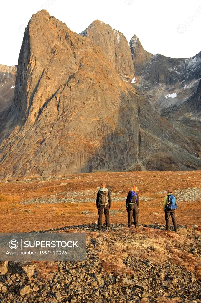 Three hikers standing on a rock pile at sunset looking at Mount Monolith in Tombstone Territiorial Park, Yukon.