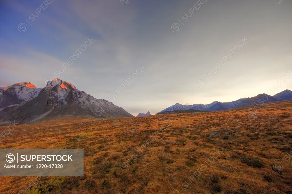 Last rays of sunlight hitting the peak of Mount Monolith with Tombstone Mountain in the distance. Tombstone Valley in the Yukon during autumn.