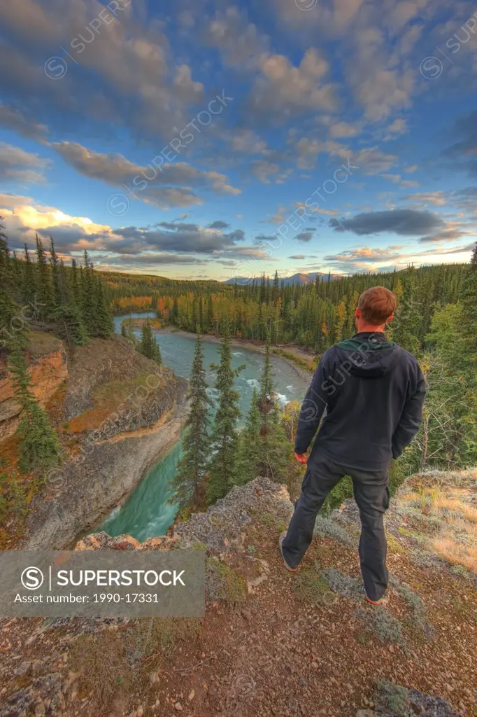 Hiker standing above the Lapie River near Ross River at sunset, Yukon.