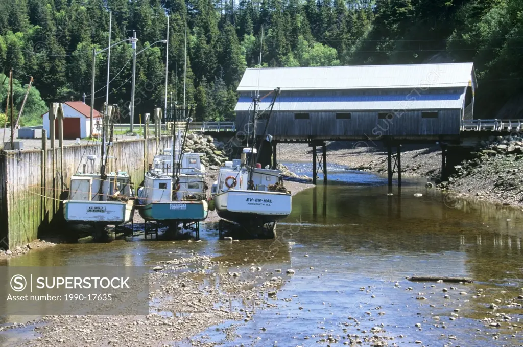 Fishing boats docked at low tide in front of covered bridge, St. Martins, Bay of Fundy, New Brunswick, Canada
