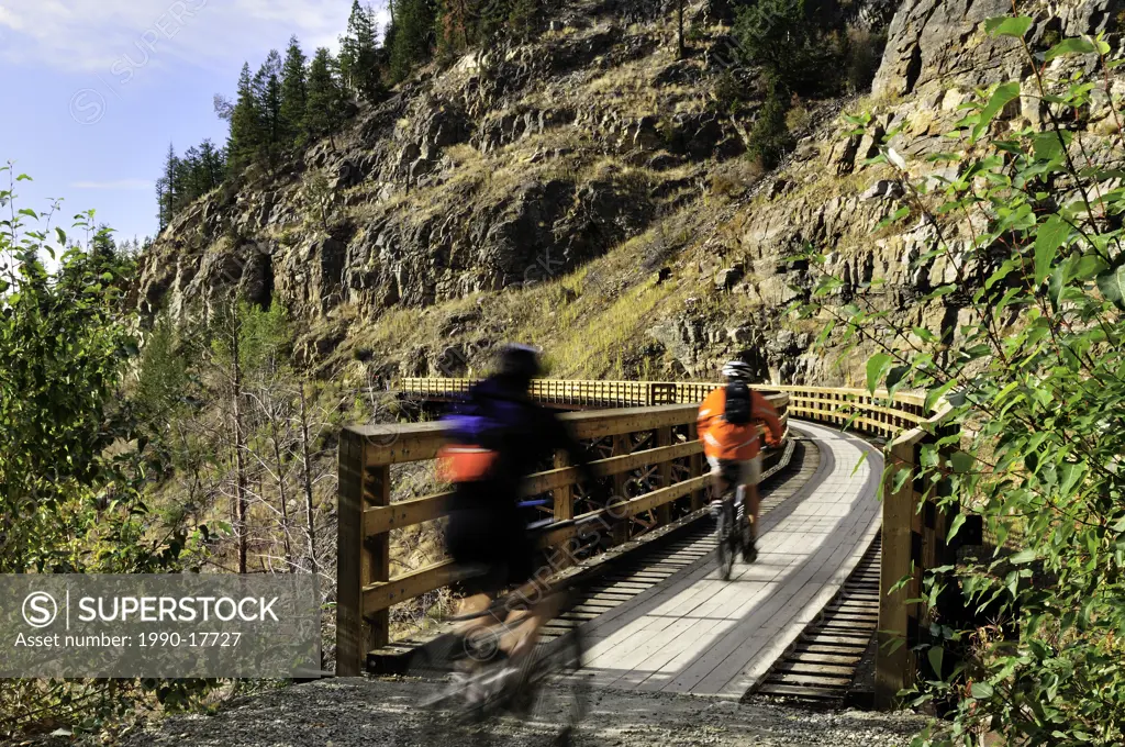 Two cyclists, blurred, cross trestle in Myra Canyon, old Kettle Valley Railway.