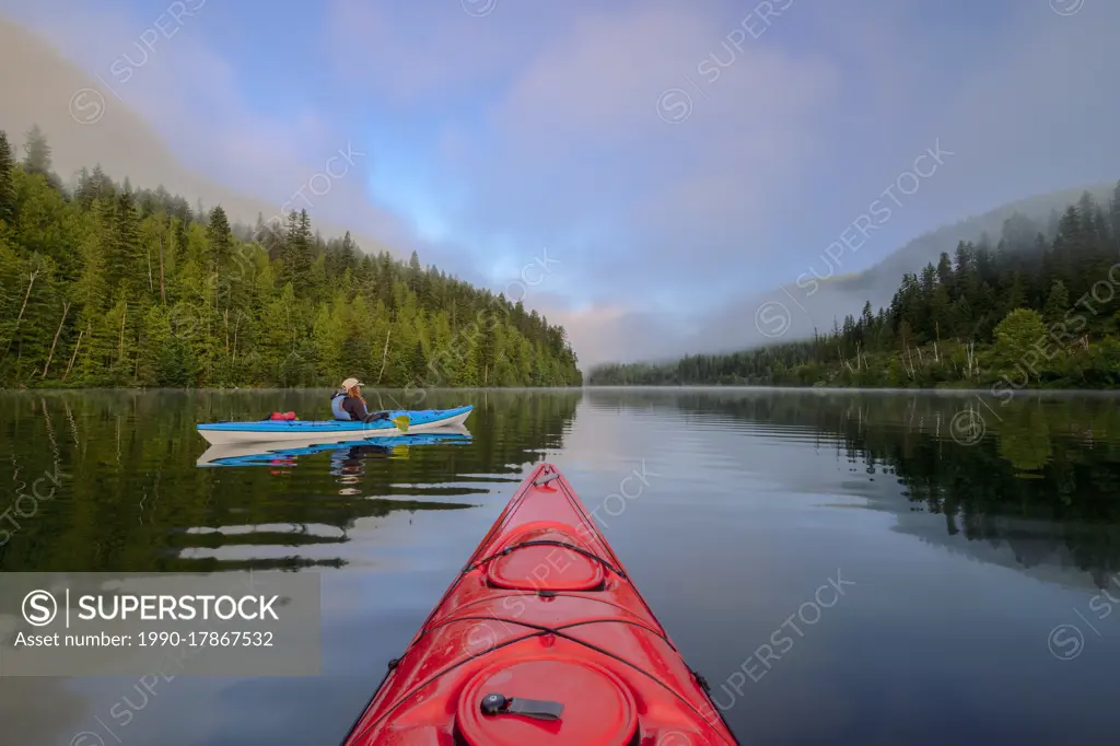 Kayakers with red and blue kayaks on Echo Lake at sunrise, Echo Lake provincial park near Lumby, British Columbia, Canada