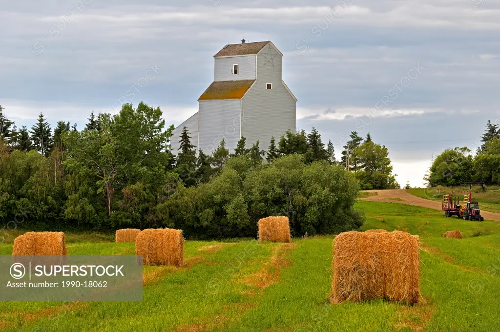 A tall grain elevator standing behind a harvested field in rural Alberta Canada