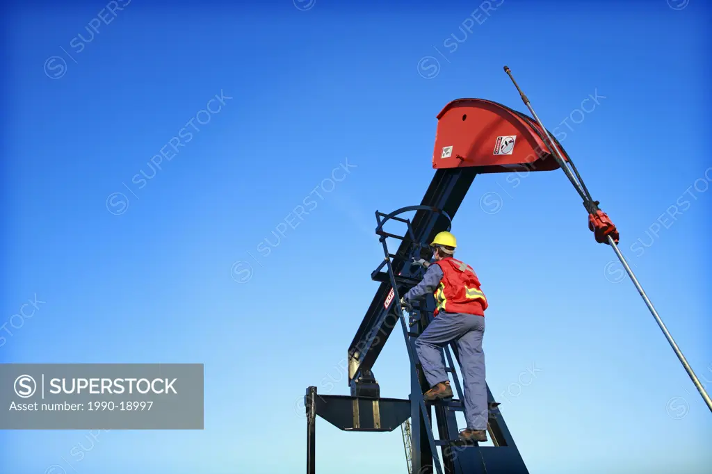 Worker climbing pumpjack, Alberta, Canada
