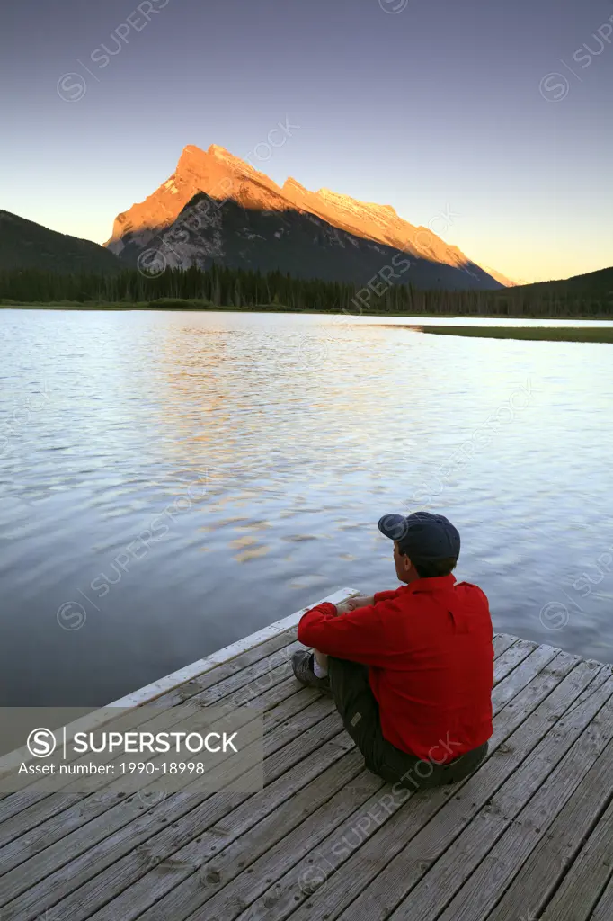 Adult male sitting on dock at Vermillion Lake at sunset with Mount Rundle in the background, Banff National Park, Alberta, Canada.
