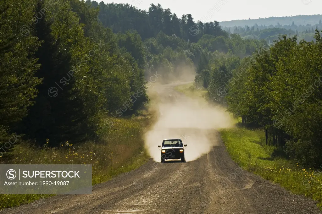 Car driving on country road through boreal forest. Riding Mountain National Park, Manitoba, Canada