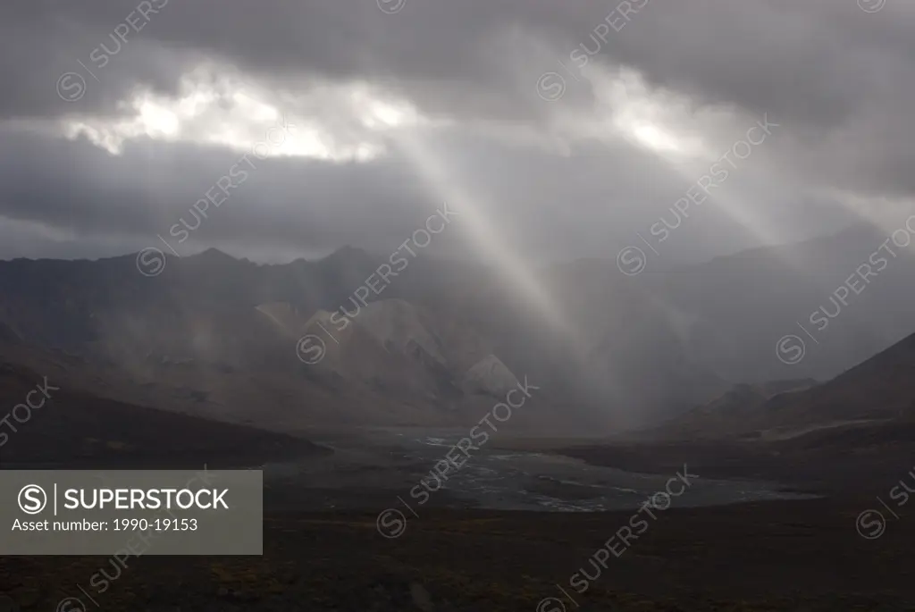 Light rays shining through rain clouds over Polychrome Pass and Toklat River Valley. Denali National Park, Alaska, North America.