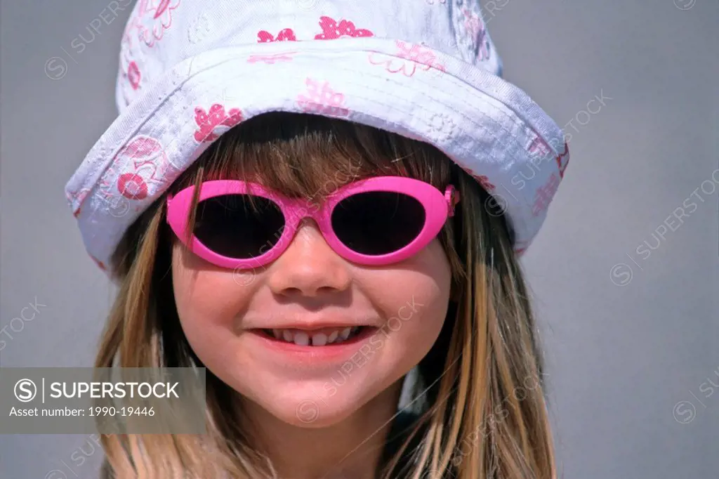 A close up portrait of a young caucasion girl in a summer hat and sunglasses with a happy facial expression