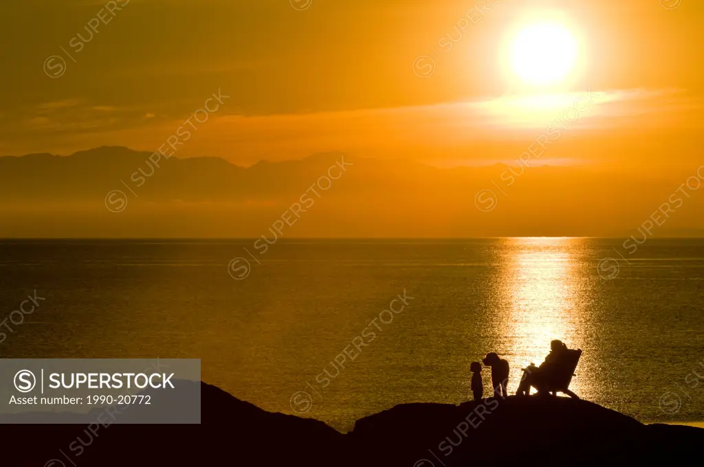 A mom and toddler are silhouetted by the sunset on an oceanside rock off Beach Drive, Victoria BC.