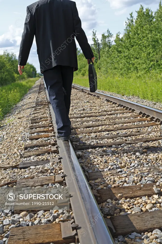 Middle age businessman walking on rail road line with briefcase in hand.