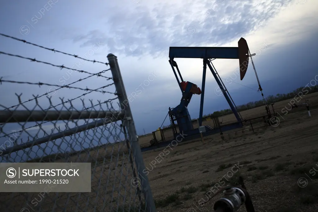 Oil pump jack in evening with fence in Alberta, Canada
