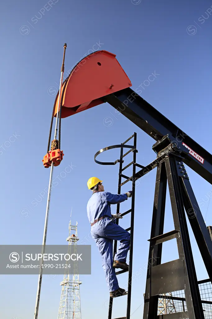 Worker climbing pump jack with oil drilling rig in background at Canadian Petroleum Discover Museum in Devon, Alberta, Canada.