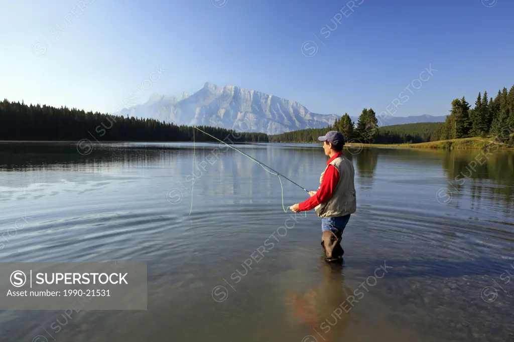 Middle age male fly fishing in mountain lake. Two Jack Lake with Rundle Mountain background, Banff National Park, Alberta, Canada.