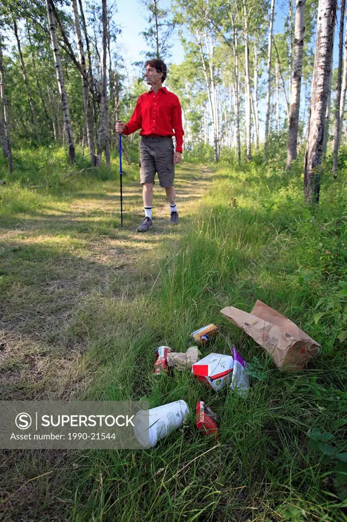 Middle age male hiking on forest trail with garbage on the ground.