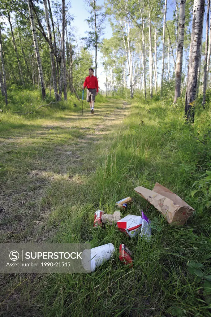 Middle age male hiking on forest trail with garbage on the ground.