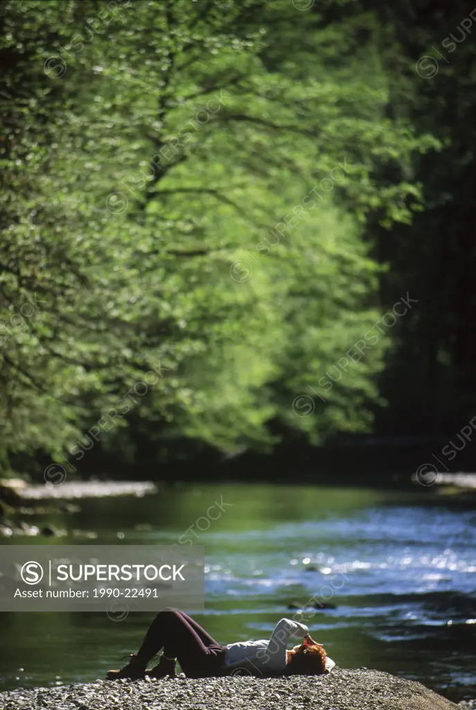 Woman sitting on gravel bar with a river flowing by, Carmanah Walbran Provincial Park, Vancouver Island, British Columbia, Canada