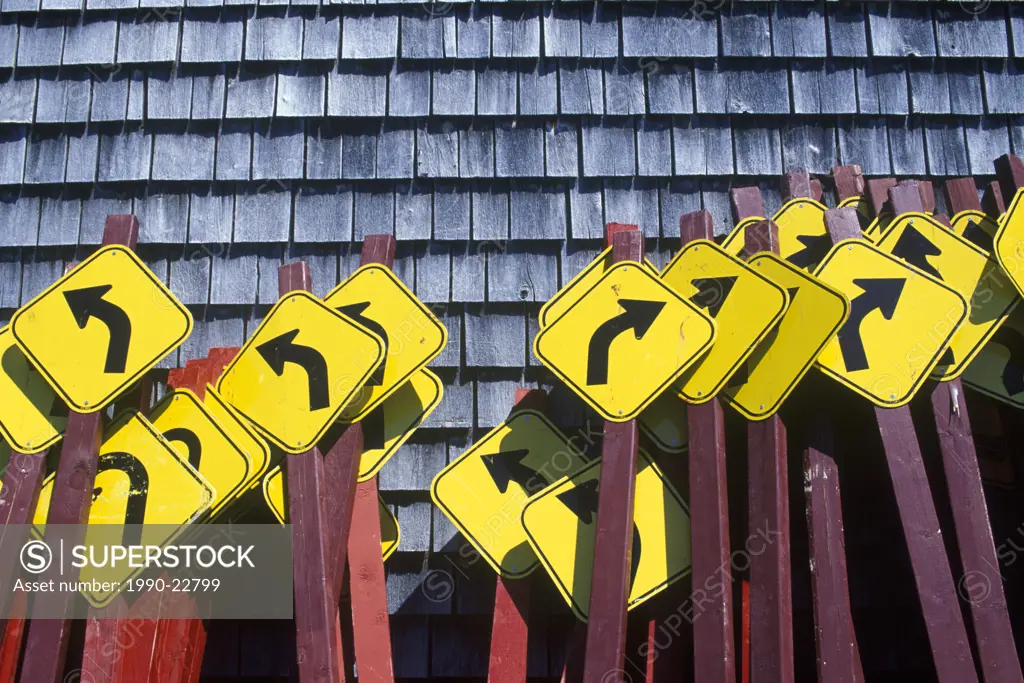Curve ahead roadsigns bunched together against cedar shingled wall, British Columbia, Canada