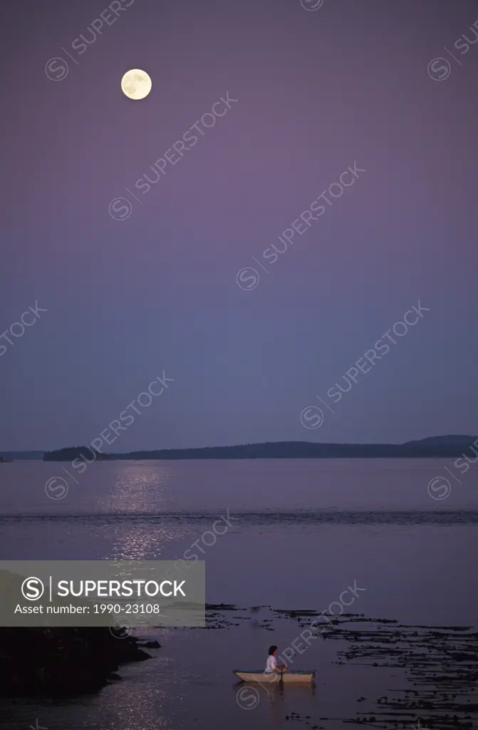 woman in small dingy in kelp bed under full moon, Gulf Islands, British Columbia, Canada
